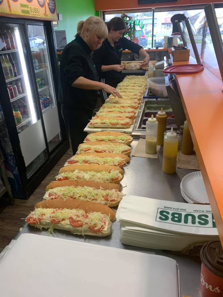 Paradise Subs staff lining up a row of fresh subs behind the counter